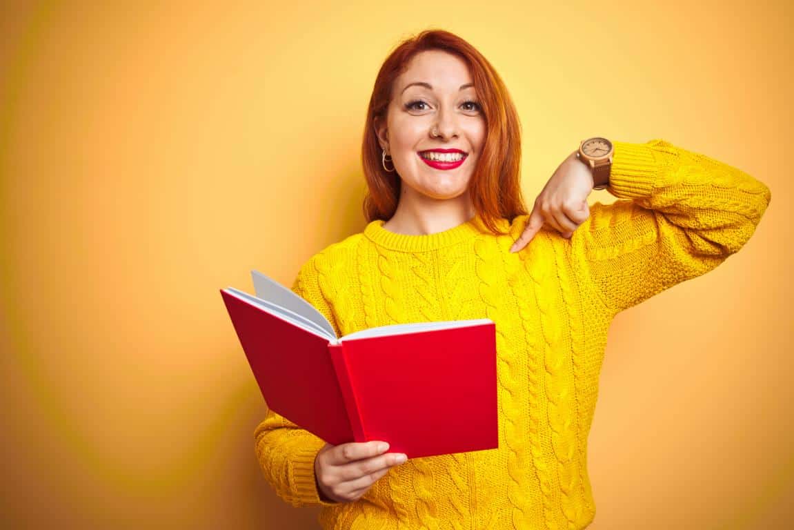 Junge rothaarige Frau zeigt begeistert auf ein Buch in ihrer Hand